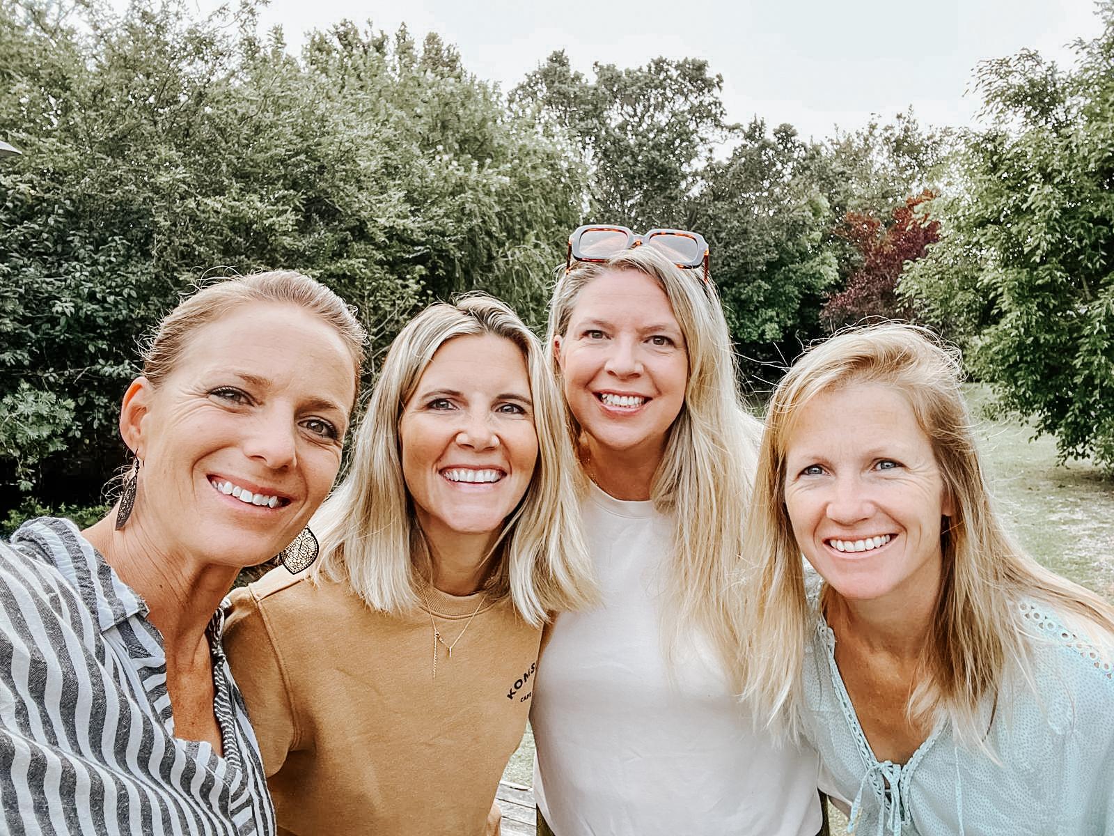 Four women smiling together for a selfie outdoors