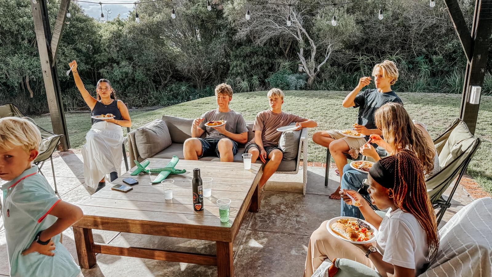 Teens and children eating together on a patio under string lights