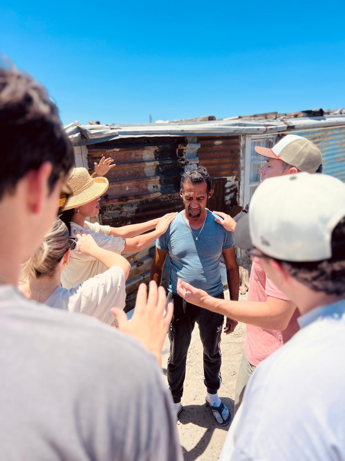 Students praying over a man during a township outreach