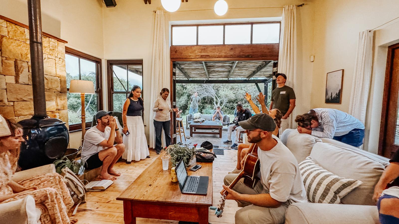 A living room full of people worshipping and praying together with a guitar