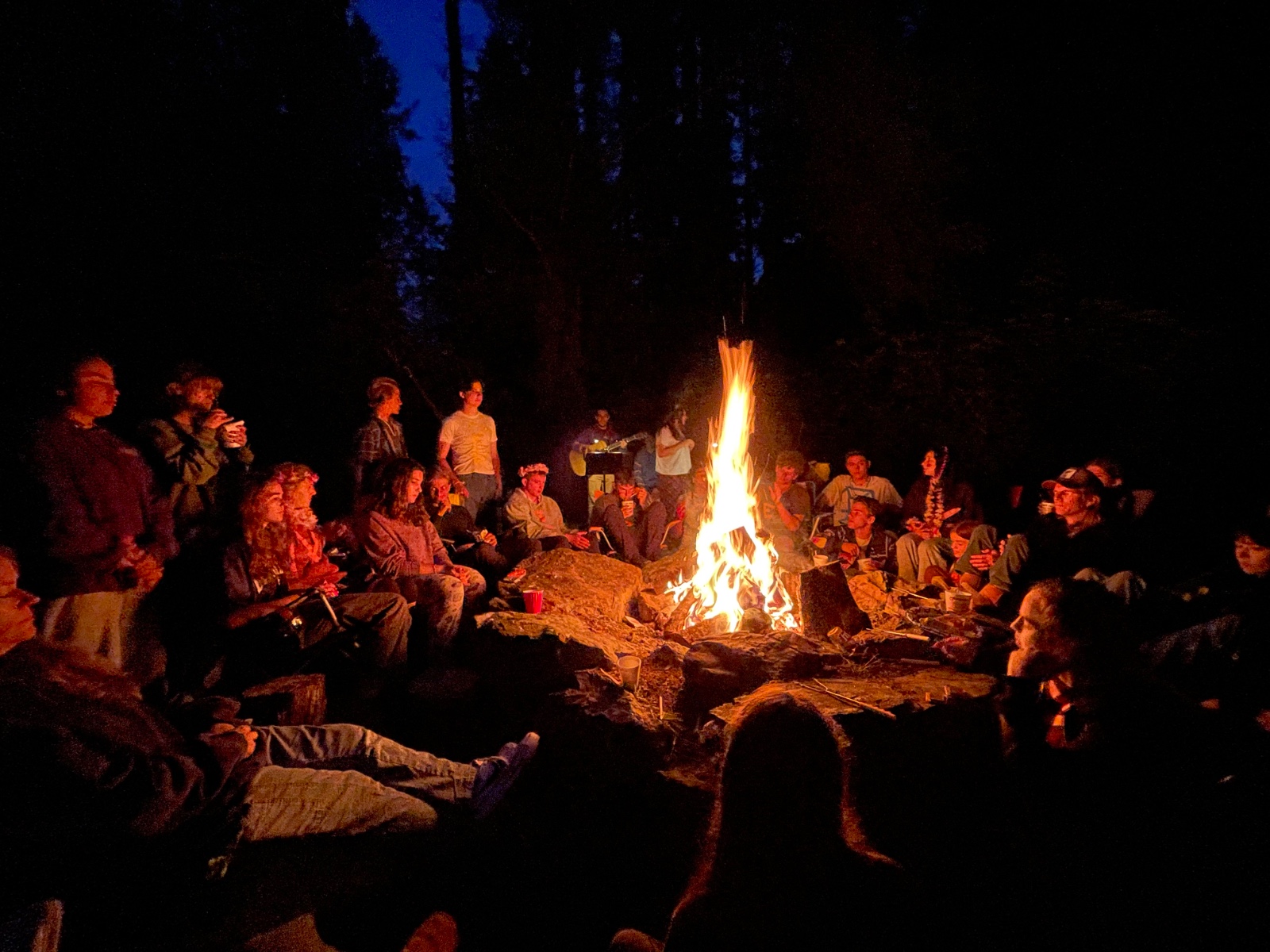 Students gathered around a blazing campfire at dusk