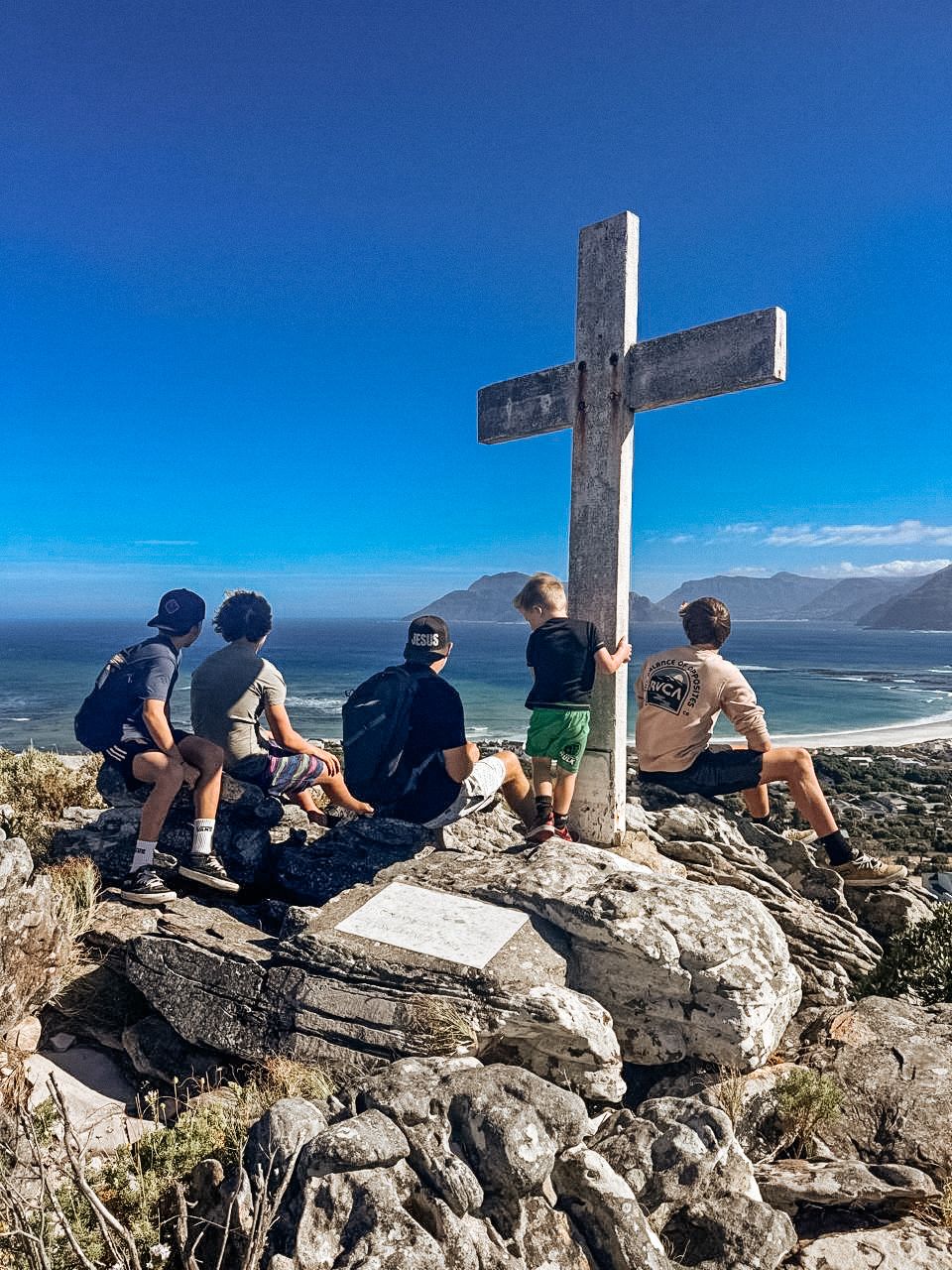Boys sitting at a hilltop cross overlooking the ocean in Cape Town